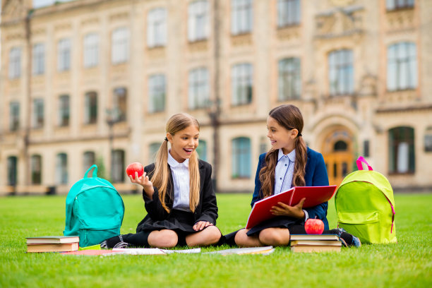 全尺寸的照片，兴奋的孩子，梳着浅棕色的头发，梳着马尾辫，看笔记本，背包，坐在户外的草地上图片下载