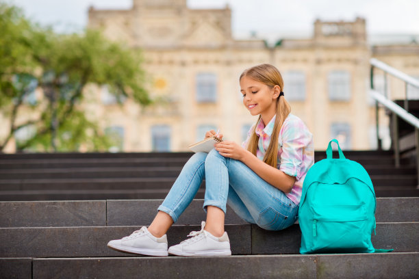 简介侧面的照片，可爱的孩子与马尾辫写穿着格子t恤牛仔牛仔裤坐在大学附近图片下载