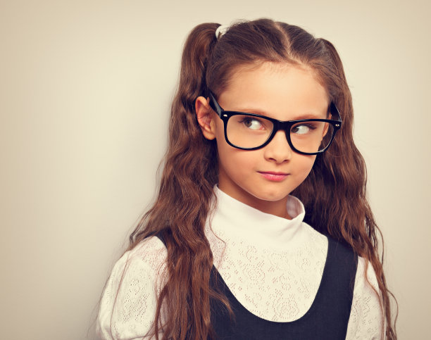 愁眉苦脸的小学生女孩与长发型在时尚眼镜在制服做有趣的面相。色调复古的彩色肖像图片下载