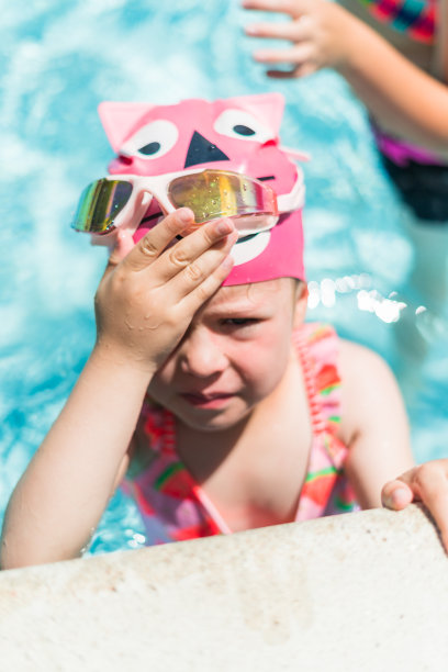 戴着粉色游泳杯和护目镜的小女孩在室外游泳池游泳图片下载