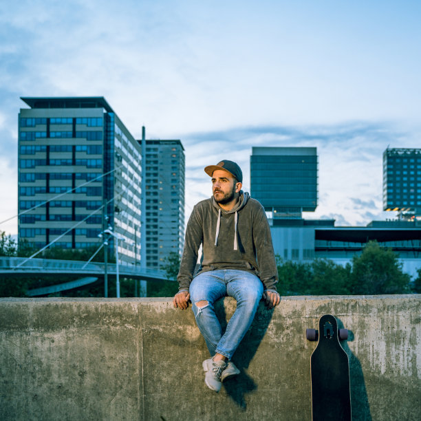 一个悠闲的男人坐在他的长板旁，欣赏着巴塞罗那的城市景色图片下载