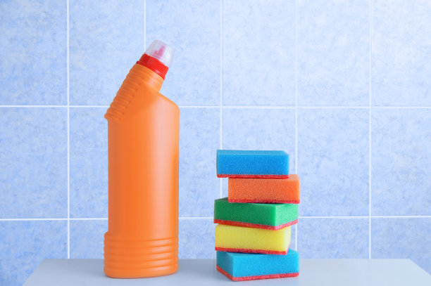 白色架子上放着一瓶洗涤剂和泡沫海绵。蓝色瓷砖的背景。图片下载