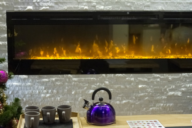 一个金属水壶和几个杯子在一张桌子靠近圣诞树的背景，一个大的电壁炉，选择性的焦点图片下载