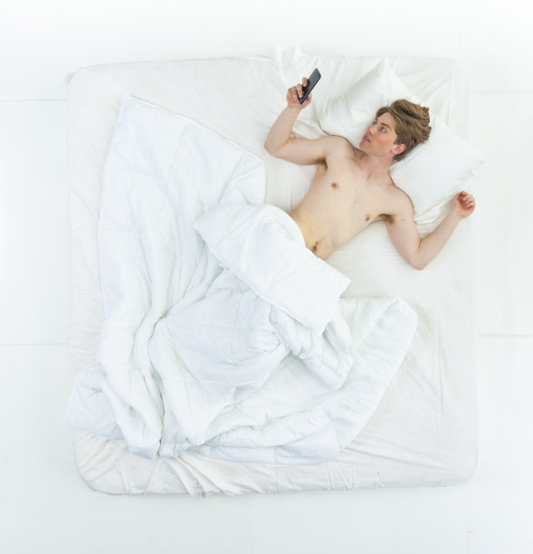 英俊的男人躺在床上，赤膊上阵，还在打电话图片下载