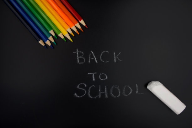 彩色铅笔和粉笔在黑板或木炭黑板上，上面用粉笔写着“回到学校”。图片下载