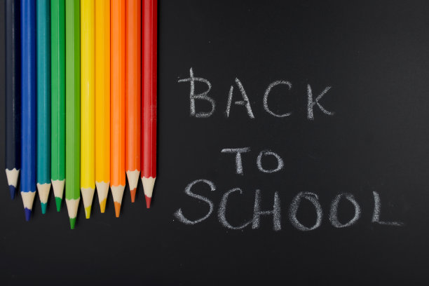 彩色铅笔在黑板/木炭黑板上，上面用粉笔写着“回到学校”。图片下载
