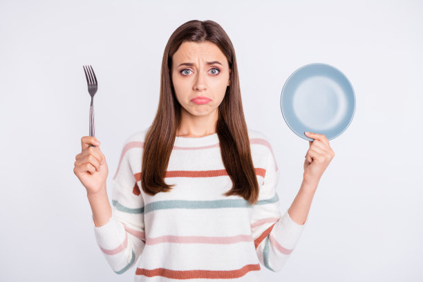 饥饿的女士拿着叉和空盘子想要更多的晚餐穿条纹套头衫孤立的白色背景图片下载