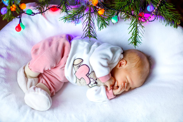一个星期大的新生儿在圣诞树旁睡觉，背景是彩色的花环灯。特写的可爱的孩子，小女孩梦想的和平。家庭，圣诞节，出生，新生命图片下载