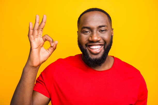 照片上的黑人男子向你展示ok标志，表明一切都是完美的，露出牙齿，而孤立与黄色背景图片下载