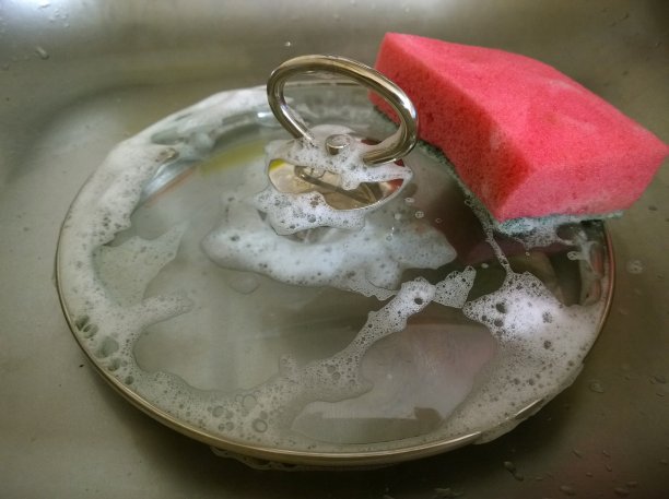 清洁和洗盘子。红海绵炖锅的玻璃盖。洗碗。洗涤剂和化学品的危害和安全概念。图片下载