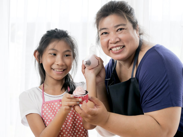 亚洲女孩学习与她的母亲准备装饰自制纸杯蛋糕，生活理念。图片下载