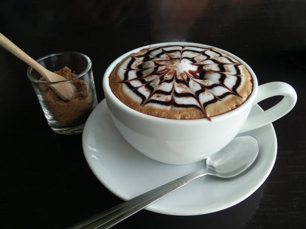 近距离的卡布奇诺或拿铁与泡沫在白色咖啡杯上的黑色木桌咖啡馆。生活方式咖啡时间，拉花艺术概念。图片下载