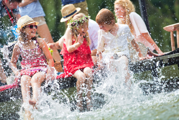 母亲和孩子们在湖里玩水的照片，而坐在码头上对着家人在湖边的夏天图片下载