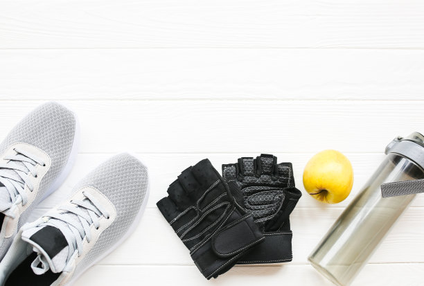 运动的照片。健康的生活方式。装水的瓶子，苹果和皮手套。时尚运动鞋。白色木制背景。完美的平面。图片下载