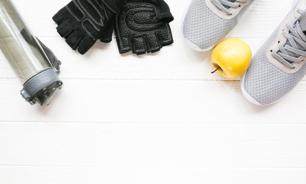 运动的照片。健康的生活方式。装水的瓶子，苹果和皮手套。时尚运动鞋。白色木制背景。完美的平面。图片下载