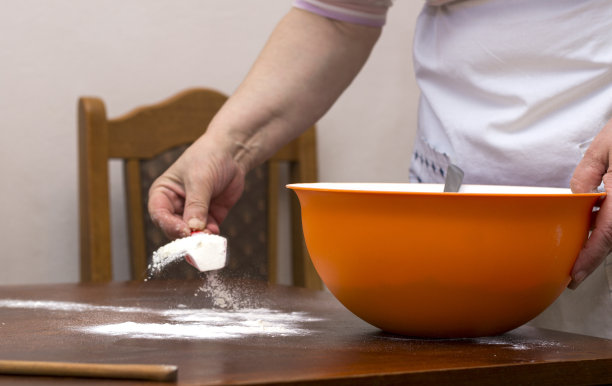 老妇人围着围裙，在铺着面粉的木桌上揉面包图片下载