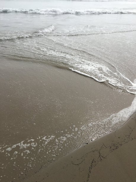 平静的波浪在棕色的沙滩上靠近图片下载