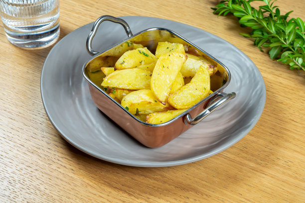 烤牛油马铃薯角与迷迭香金碗。关闭了。素食食物。美味的装饰。有选择性的重点。食谱或菜单的食物照片。街头食品图片下载