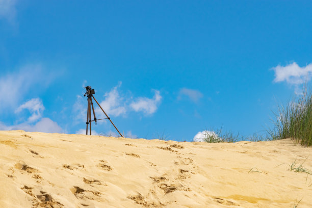 带智能手机的三脚架在沙丘上，背景是草地和蓝天。拍摄延时视频的概念。水平，文本空间。图片下载