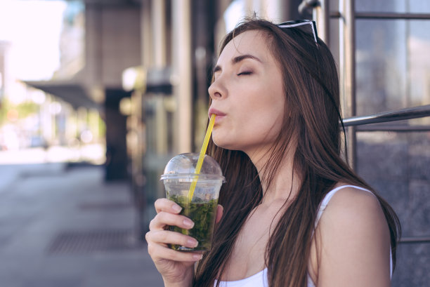 绿色新鲜水果健康天然冰沙，天气炎热，学生饥肠辘辘的理念。侧影转近观看照片肖像美丽迷人迷人的高兴女士拿着玻璃在手里图片下载