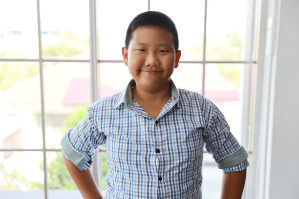 可爱的小学生男孩站在蓝色的衬衫和快乐的笑脸图片下载