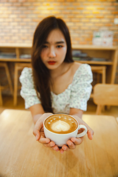 亚洲女人拿着一杯热拿铁艺术在咖啡馆。图片下载
