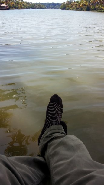 在印度喀拉拉邦，穿着袜子和裤子的腿对着绿色的湖水，作为背景和标题。喀拉拉邦旅游业。为文本复制空间。图片下载