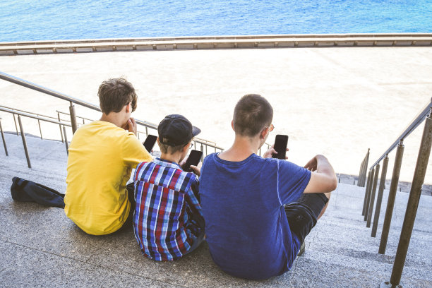 一群年轻人坐在学校外面。时髦的快乐男孩享受新的潮流技术一起分享社交媒体上的照片和视频在线。青年科技团结和z世代概念图片下载