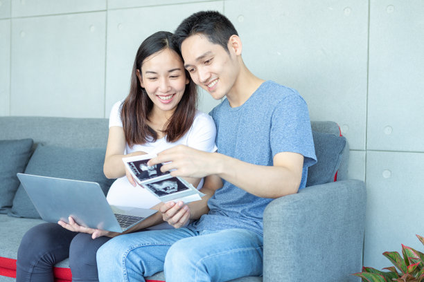 超声波怀孕的妈妈和爸爸。开心的孕妇带着丈夫展示自己宝宝的扫描图和笔记本电脑。幸福的夫妇正拿着宝宝的超声波照片。图片下载