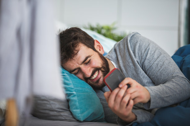 男人在床上玩智能手机时大笑图片下载