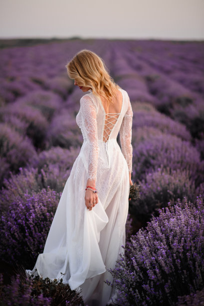 在夕阳下，年轻的女人穿着白色的裙子走过盛开的薰衣草田图片下载