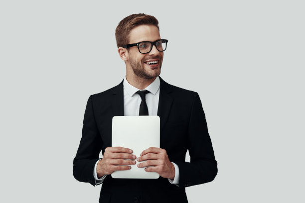 英俊的年轻男子穿着正装看着别处和微笑，而站在灰色的背景图片下载