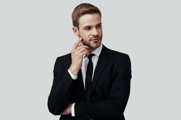 英俊的年轻男子穿着正装望着别处，而站在灰色的背景图片下载