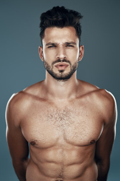 英俊年轻的赤膊男子看着相机，而站在灰色的背景图片下载