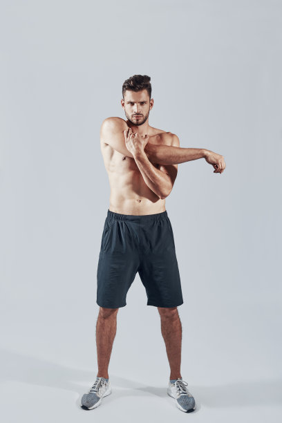 全身英俊的年轻男子在运动服装暖身，而站在灰色的背景图片下载