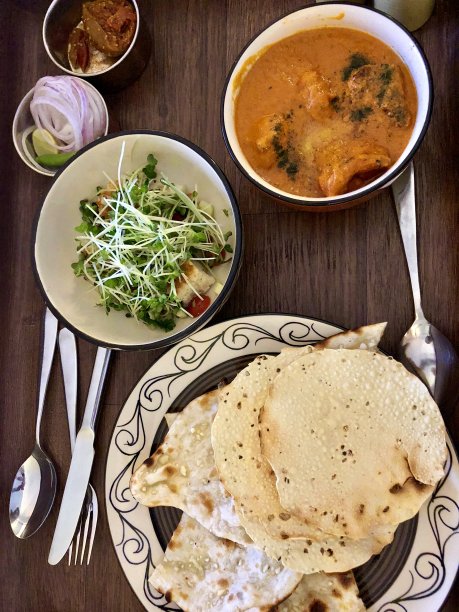 桌上的碗里放着黄油鸡肉食谱，传统的咖喱鸡酱可以吃了，配上辛辣的咖喱酱、奶油/酸奶凝乳、香草和香料，配上馕饼、pappadom、绿色沙拉和泡菜图片下载