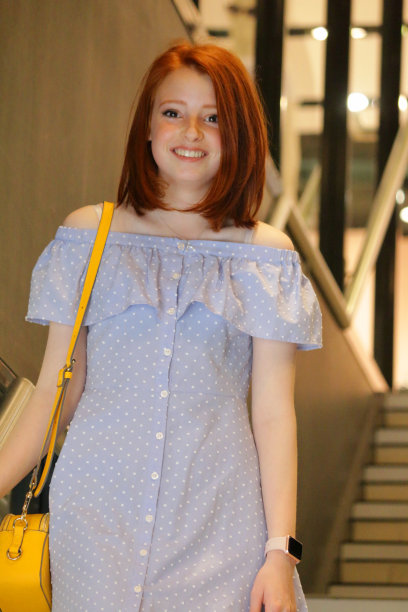 这是一个14 / 15岁的红发少女走下商店楼梯的照片，她穿着一件漂亮的淡蓝色休闲装，带有白色圆点花纹，肩上挎着一个黄色的手提包图片下载