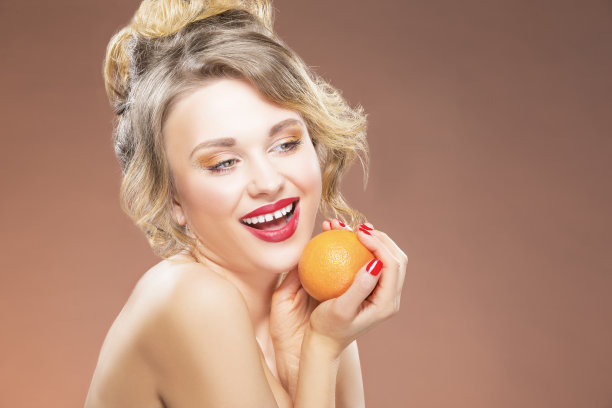 性感好玩的白人金发女孩与一个橙色水果在手中。在彩色背景下摆姿势。水平图像组成图片下载