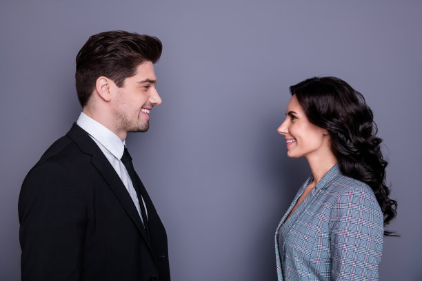 个人资料侧面的照片迷人的商务人士与深色头发卷曲的发型看起来站面对面穿着黑色的礼服夹克夹克孤立在灰色的背景图片下载