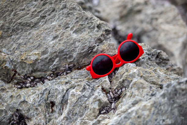 红色的太阳镜放在海边的岩石上。图片下载