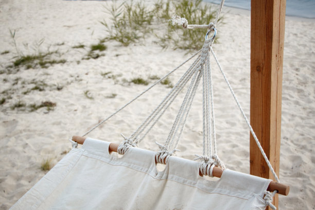 一张由天然织物制成的白色吊床的特写，在一个木制底座上挂在沙滩上的绳索上，这是自然放松的概念图片下载