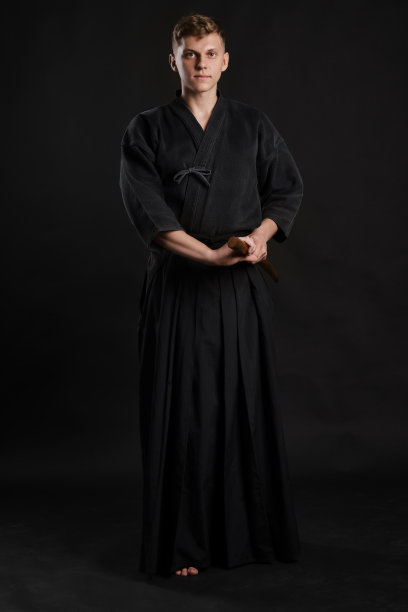 剑道大师穿着传统的日本和服正在练习武术与shinai竹剑在一个黑色的工作室背景图片下载