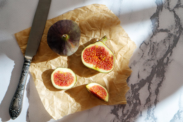 俯视图新鲜异国情调切半无花果在工艺纸大理石桌子。食物的照片背景。整个和切片无花果的创意方案。平的。从以上观点。夏天美味的果子图片下载