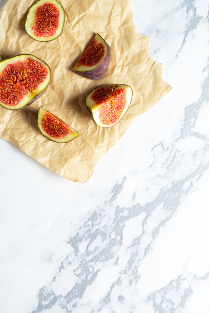 俯视图新鲜异国情调切半无花果在工艺纸大理石桌子。食物的照片背景。整个和切片无花果的创意方案。平的。从以上观点。夏天美味的果子图片下载