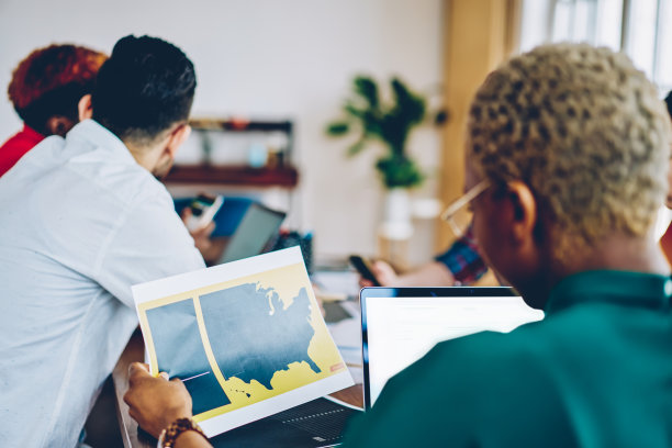 深色皮肤的女性领导手持纸插图和图形数据坐在笔记本设备，与团队的年轻人在办公室进行头脑风暴会议合作的后视图图片下载