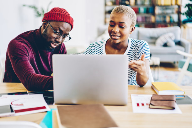 年轻的非洲裔美国人夫妇通过笔记本电脑在网上购物，在家里讨论商品，黑皮肤的男性和女性潮人互相聊天，看网上的照片图片下载