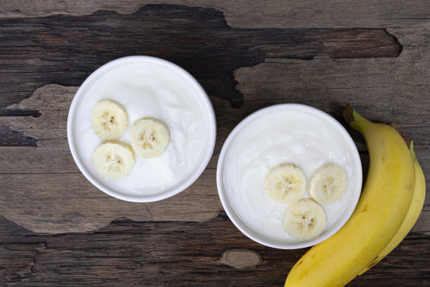 从俯视图看，木头背景上的玻璃杯里的酸奶和香蕉。图片下载