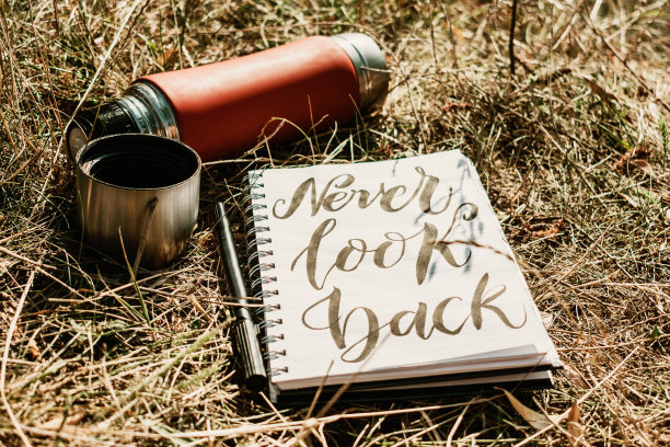 永远不要回头看在绿色草地上用钢笔和红色杯子写在白色笔记本上的单词。户外概念手写体“永不回头，无悔”图片下载