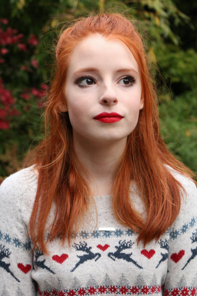 美丽的年轻女人的形象少女模特红姜黄色头发在一半的发型和迷人的化妆户外在国内的花园，漂亮的少年穿着圣诞套头衫与戏剧性的红色口红和青铜眼影图片下载