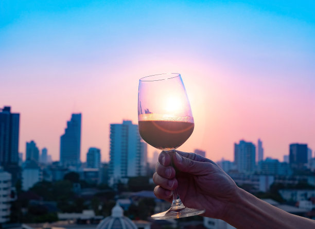 在日落城市的背景下，在酒吧餐厅的屋顶上，男人用红酒倒入玻璃杯的幸福时刻图片下载